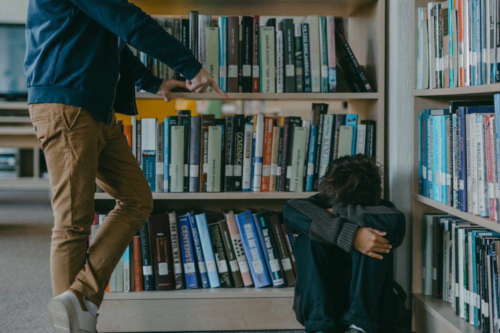 a person in black jacket sitting on the corner beside white wooden bookshelves